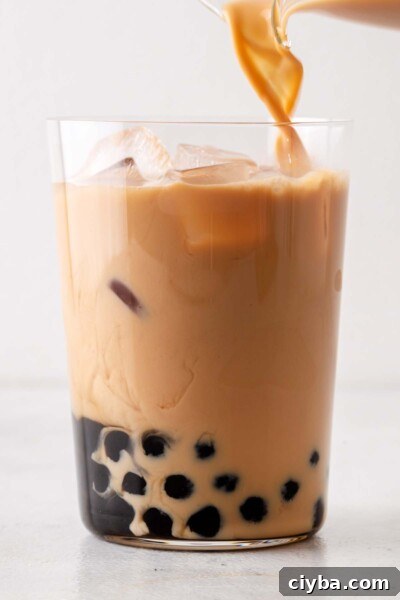 Pouring tea into a cup with ice and tapioca balls.