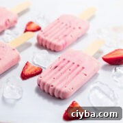 Low carb strawberry cream popsicles on white background with sliced berries and ice cubes.
