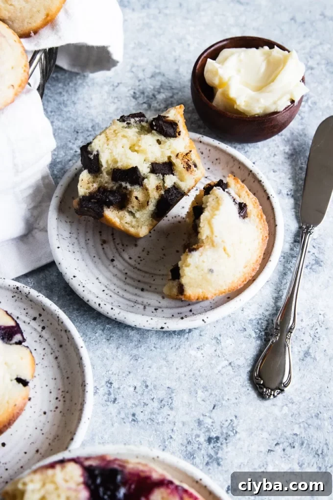 Sourdough chocolate chip muffin broken apart on a plate with butter and a knife in the background.