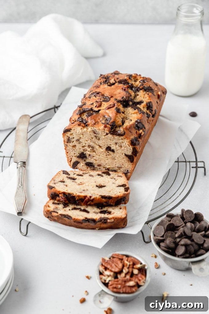 A loaf of sourdough banana bread on a surface. It has been sliced and has pecans and chocolate chunks in bowls surrounding it.