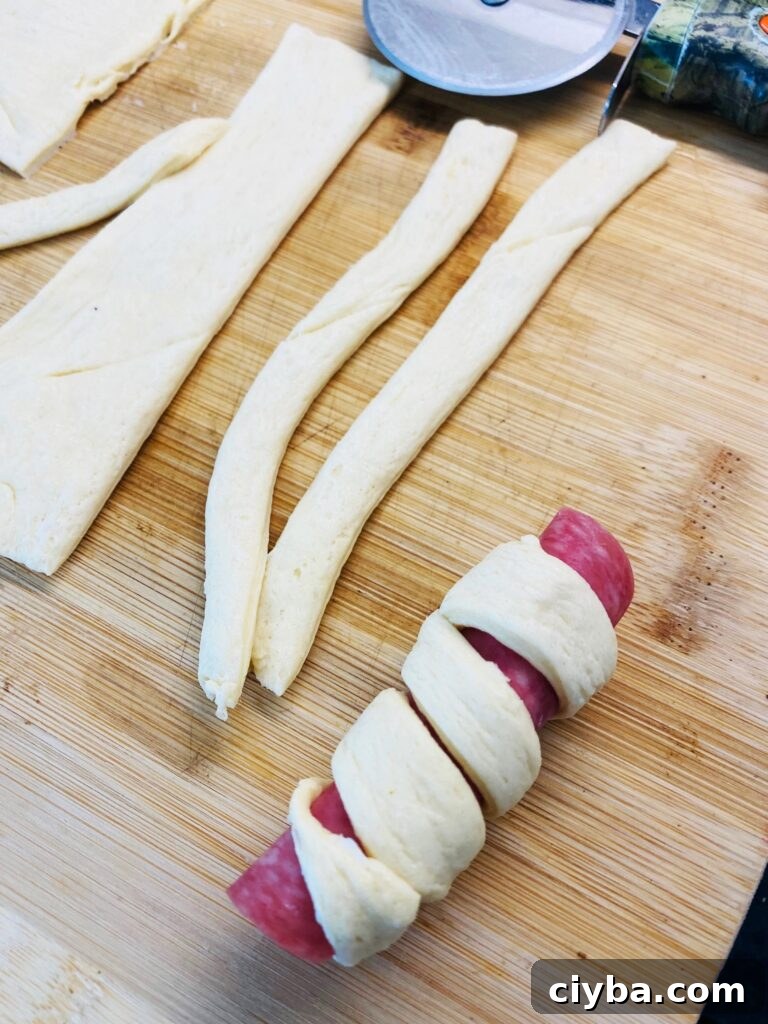 rolling a strip of crescent dough in a spiral around salami roll