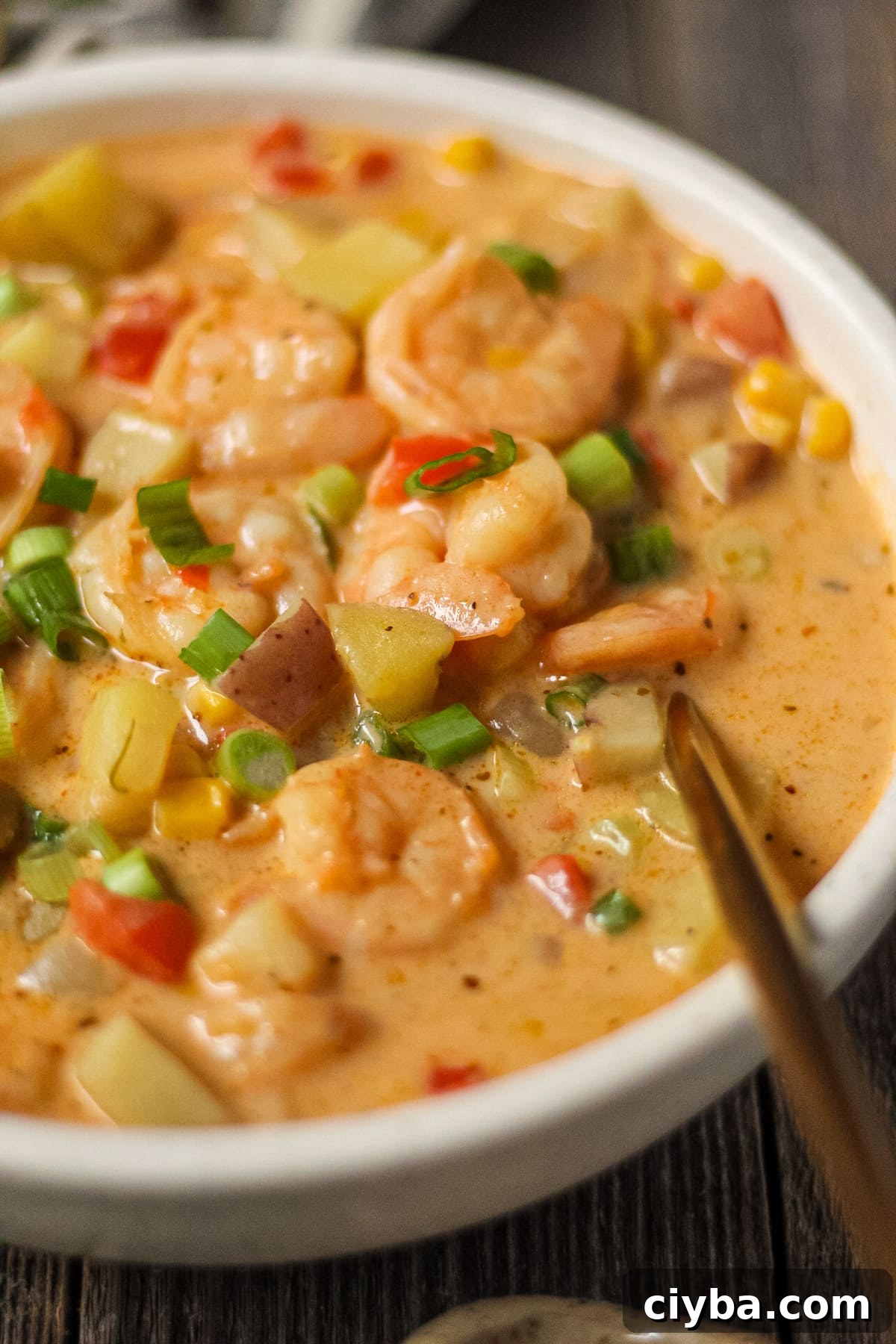 Creamy Cajun Shrimp and Corn Chowder Recipe 9 side angle shot of creamy cajun shrimp and corn chowder in a white bowl on a wooden surface. Bowl of salt and chopped green onions in top left and bottom right of shot.