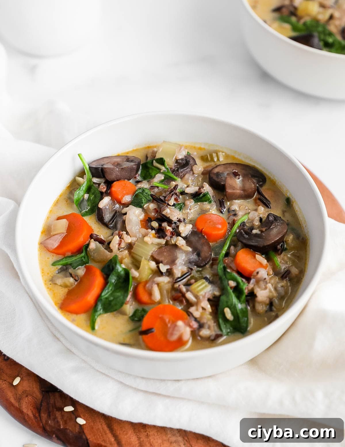 A bowl of vegetable and rice soup with mushrooms, carrots, spinach.