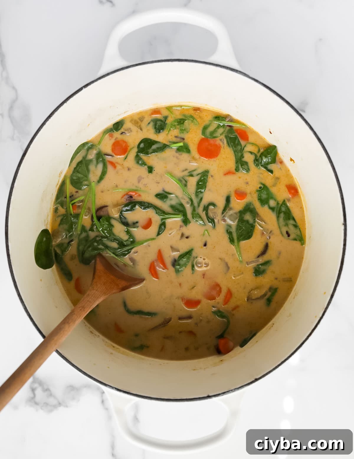 A white pot filled with a creamy vegetables soup.