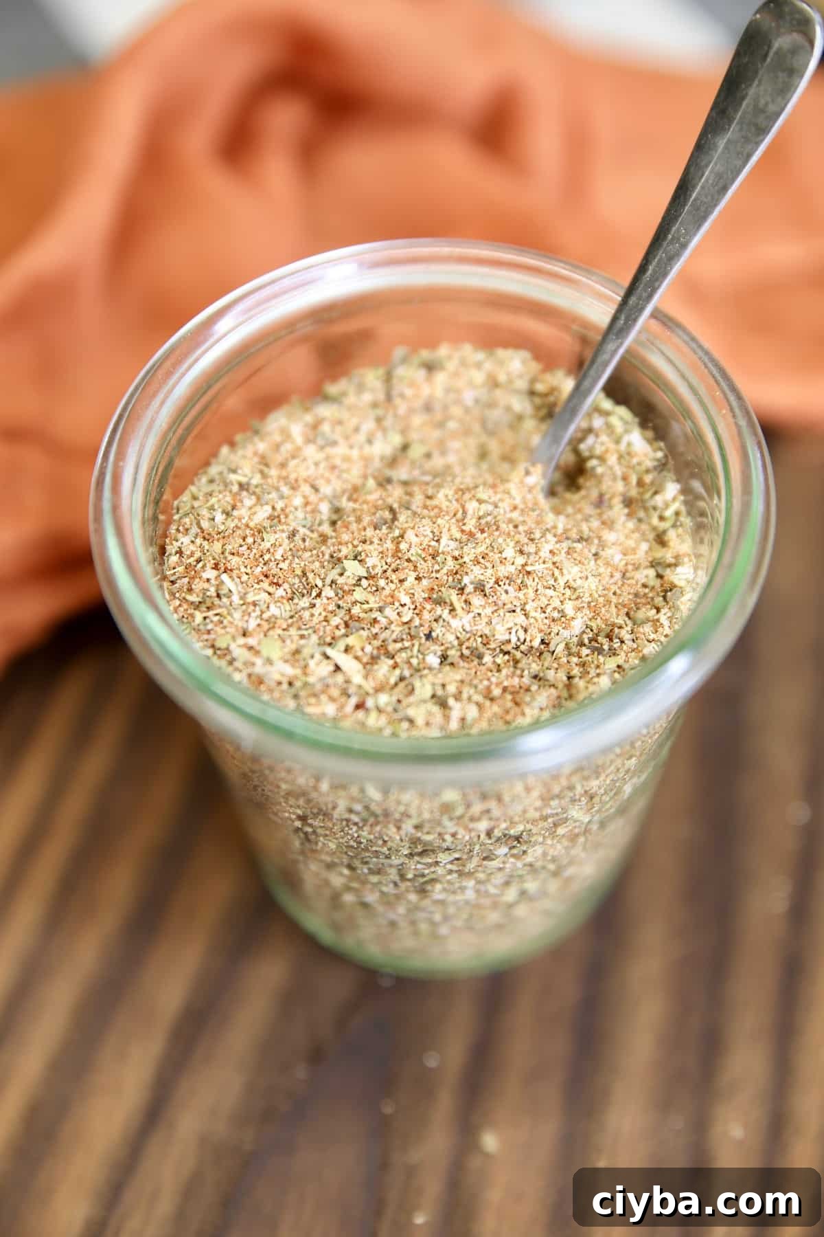 Jar of spice rub on a board with spoon in the jar.