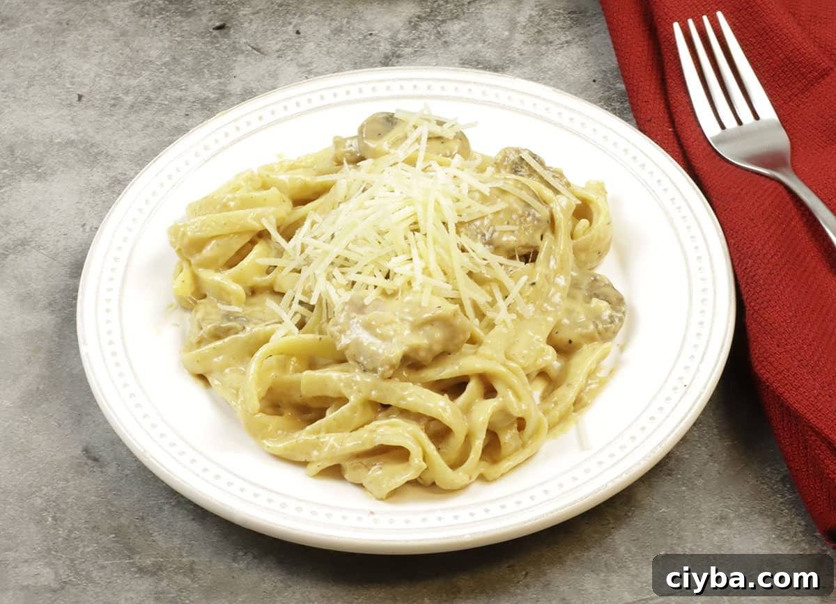 tetrazzini topped with parmesan cheese in white round plate with red napkin and fork on the side