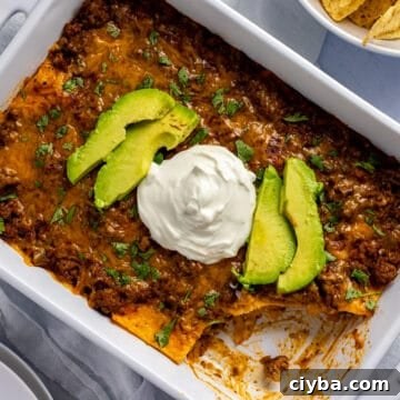 baked casserole in white rectangular dish. Topped with avocado slices and dollop of sour cream. One serving missing from casserole.