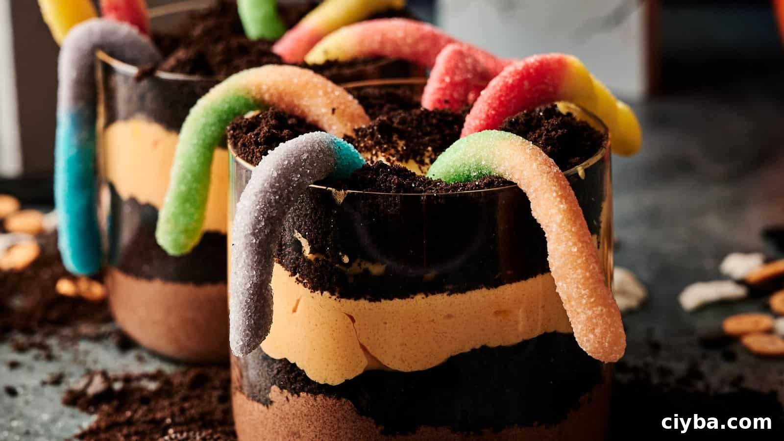 A close-up of dessert cups layered with chocolate, cream, crushed cookies, and topped with colorful gummy worms.