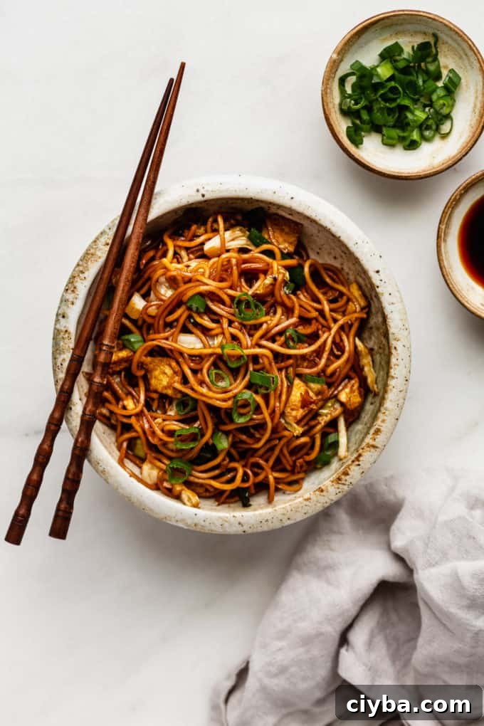 Mie goreng noodles in a bowl with a grey napkin and a small bowl of green onions on the side