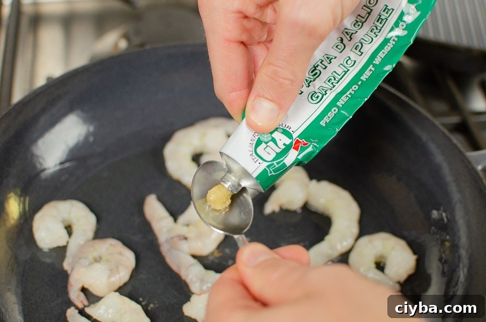 Gia garlic puree being squeezed into a teaspoon to go into a dish with king prawns cooking 