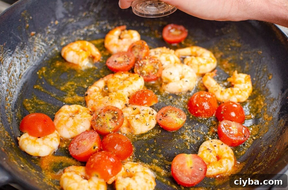 King prawns and cherry tomatoes cooking in a cast iron dish with black pepper being sprinkled ontop