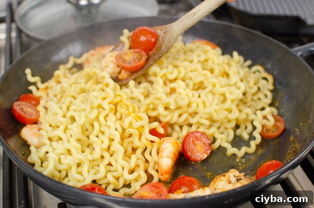 Pasta has been added to the cast iron dish with the tomatoes and king prawns