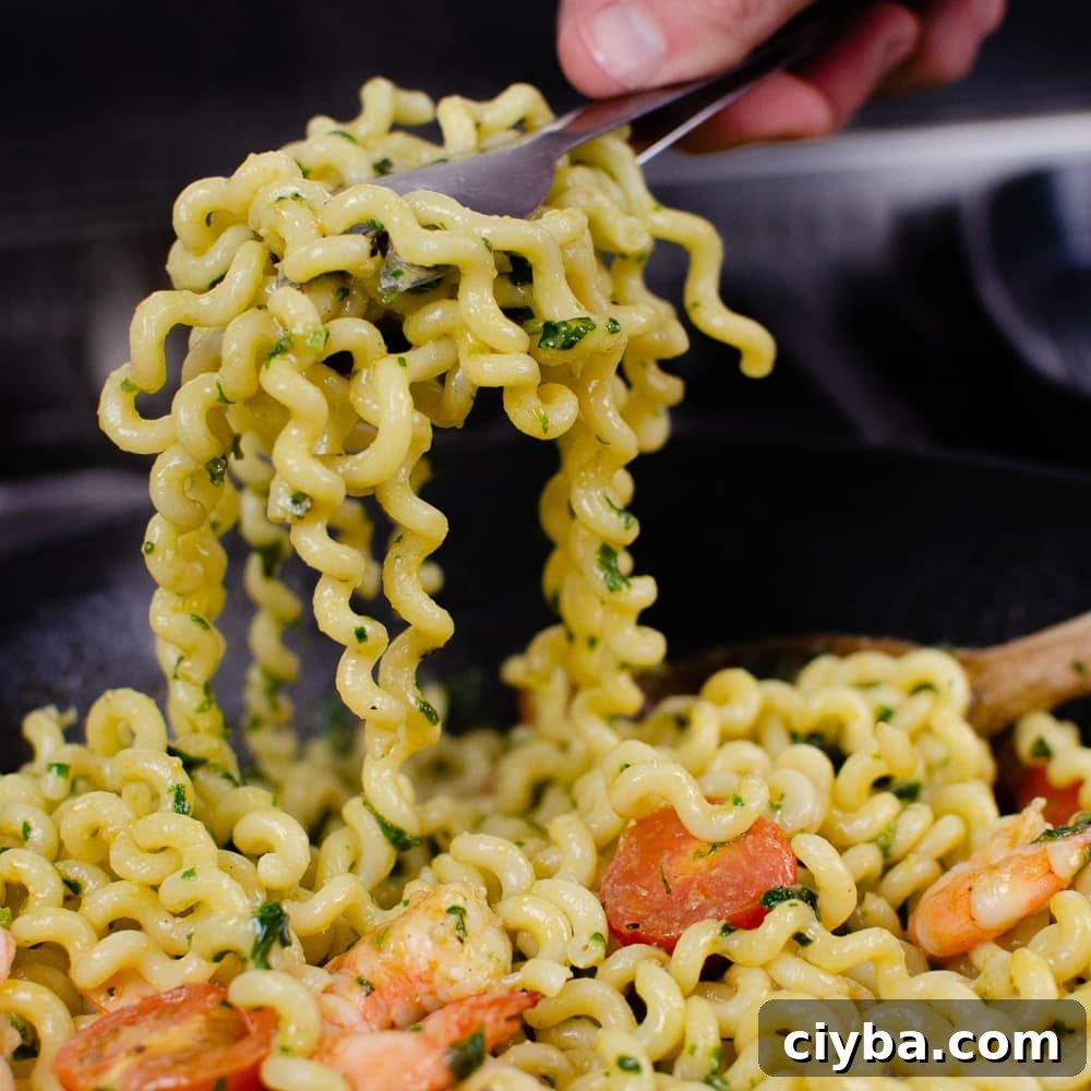 Pesto King Prawn Pasta, fusilli lunghi with prawns and tomatoes being served up with silver tongs