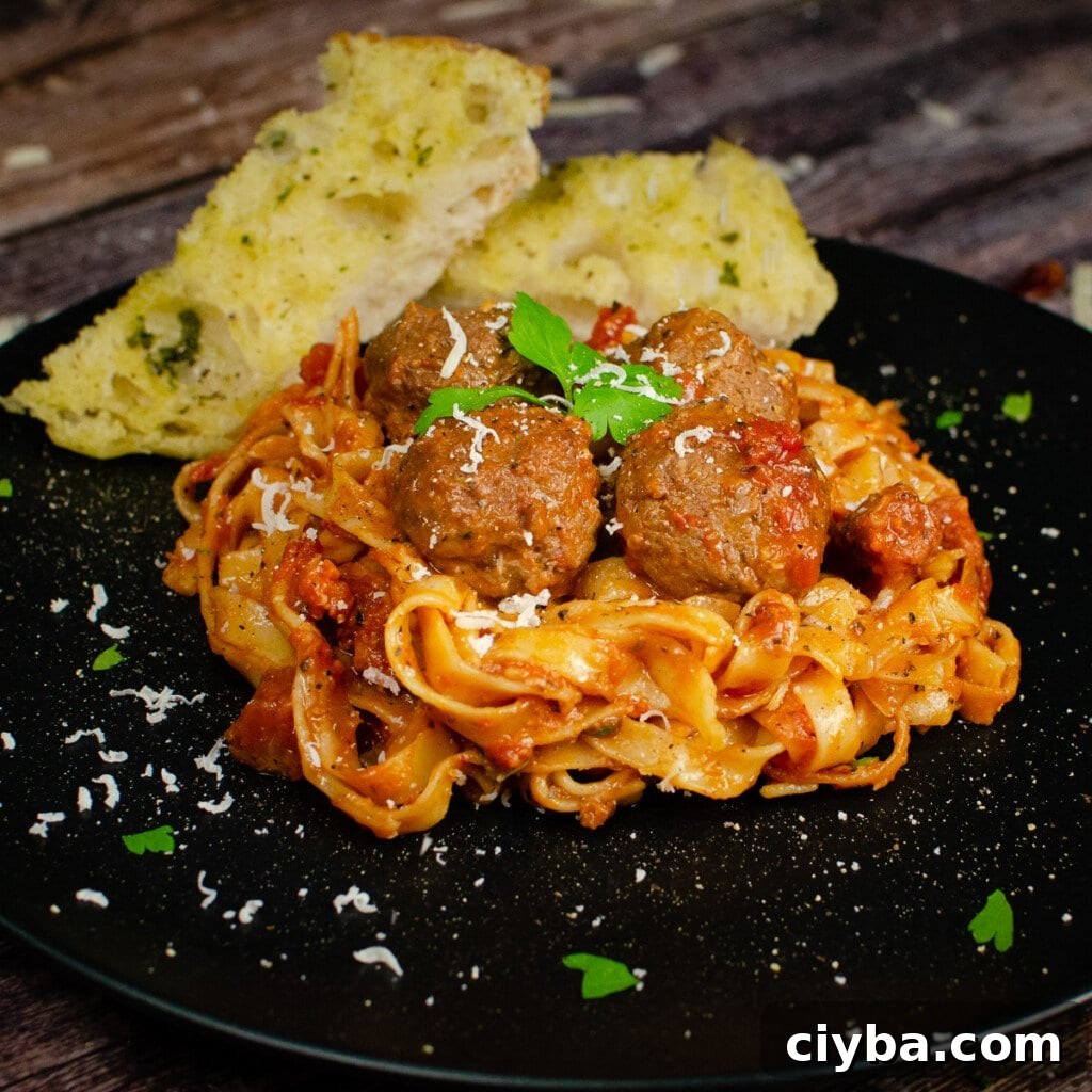 Spicy Meatball Pasta served on a black plate with garlic bread on the side