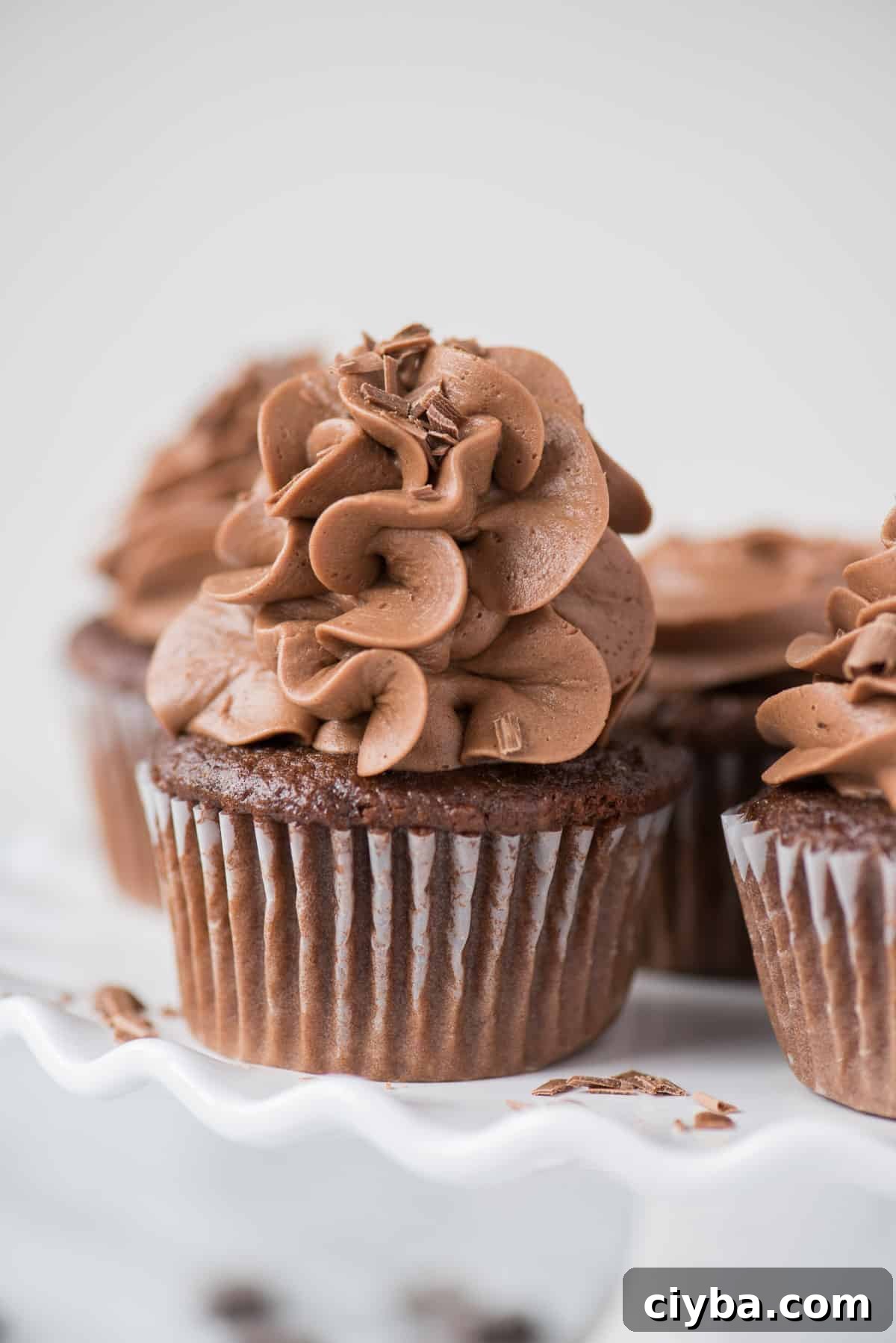 Bakery style “doctored up” chocolate cupcakes! This is an easy, one bowl chocolate cake mix cupcake recipe without pudding or coffee. #chocolate #cupcakes #cakemix #cakemixcupcakes #doctoredupcake #easycupcakes chocolate cupcakes with chocolate frosting on white plate