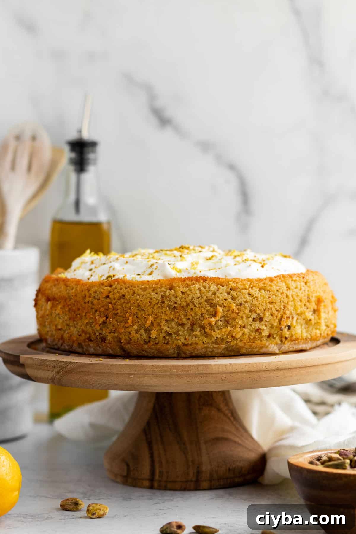 lemon pistachio cake with whipped cream on a wood cake stand