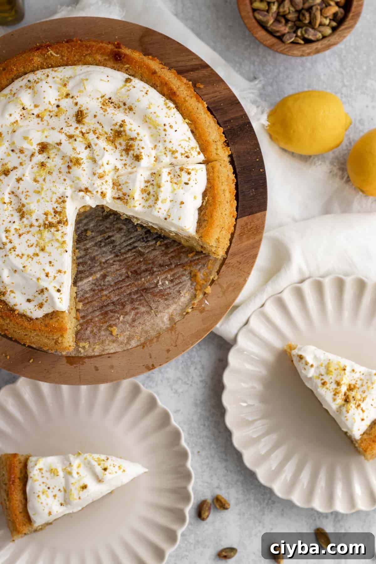 lemon pistachio cake on a wooden cake stand with 2 slices cut and on cream colored plates