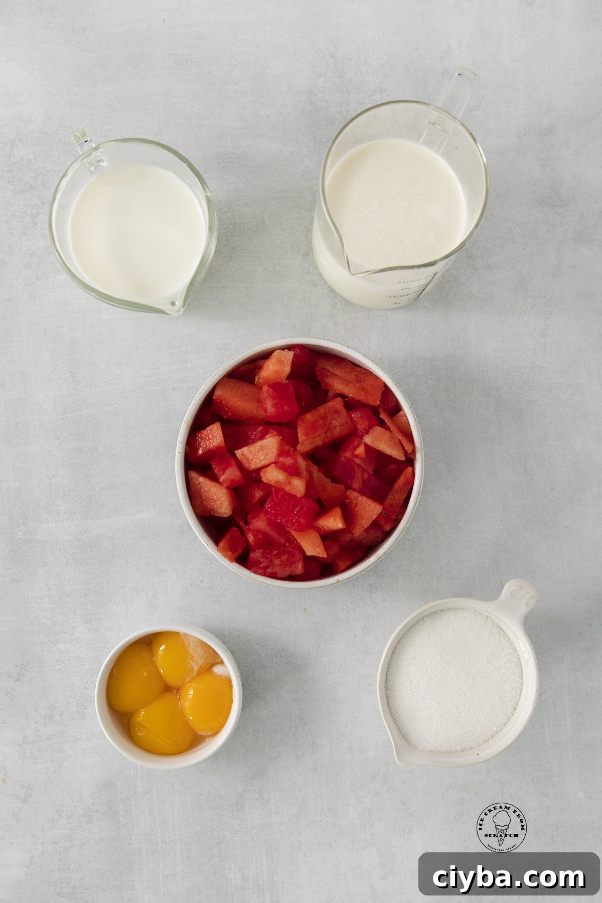 A bowl of diced watermelon next to milk, cream, egg yolks, and sugar - the ingredients for making homemade watermelon ice cream.