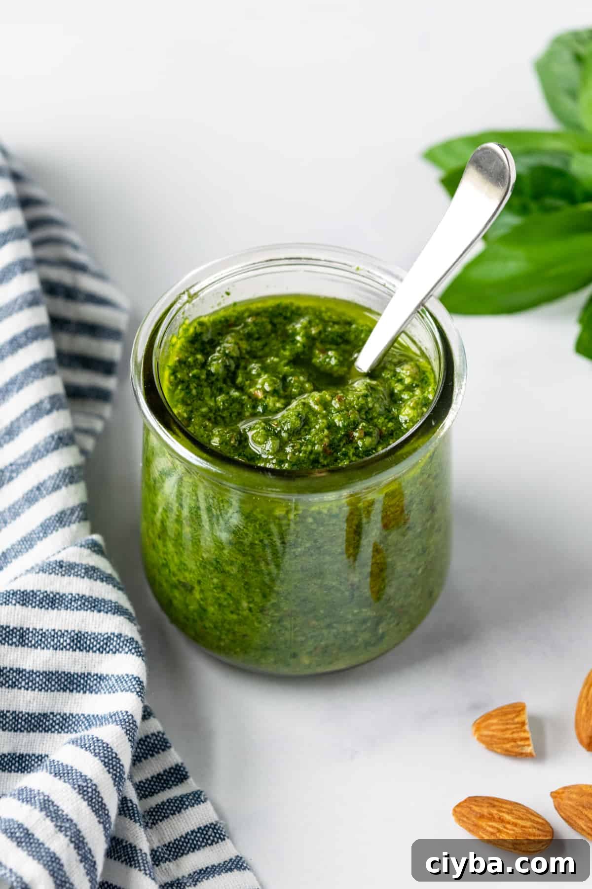 Almond Basil Pesto in a glass jar on a table with almonds scattered around it.