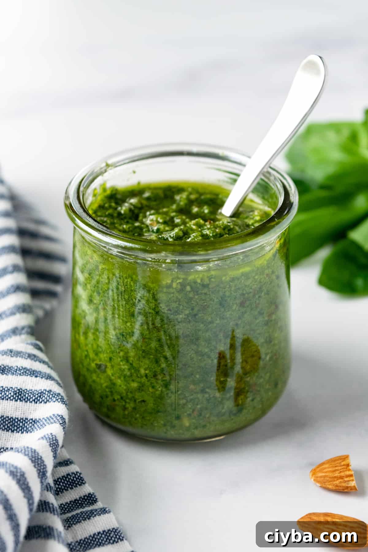 Almond Basil Pesto in a glass jar with a spoon it it.