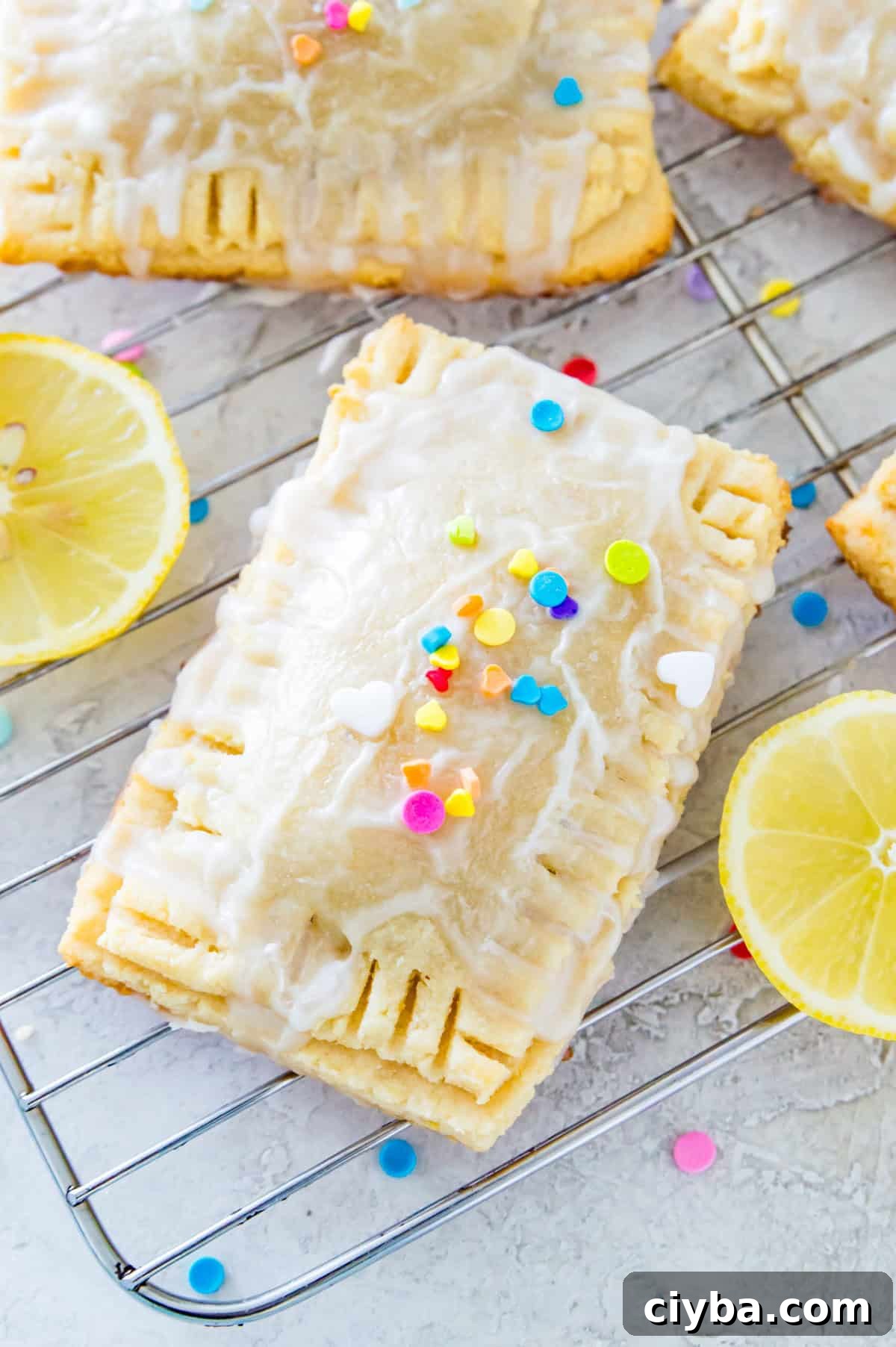 Lemon pop tarts covered in rainbow sprinkles on a wire cooling rack surrounded by lemon slices.