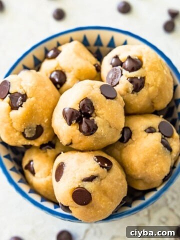 A bowl full of edible chocolate chip cookie dough bites with chocolate chips around the bowl.
