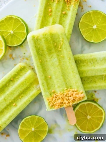 Four key lime pie popsicles stacked on top of each other with lime wedges around them.
