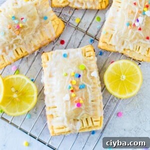 Four lemon pop tarts topped with colourful sprinkles on a wire rack with lemon slices beside them.