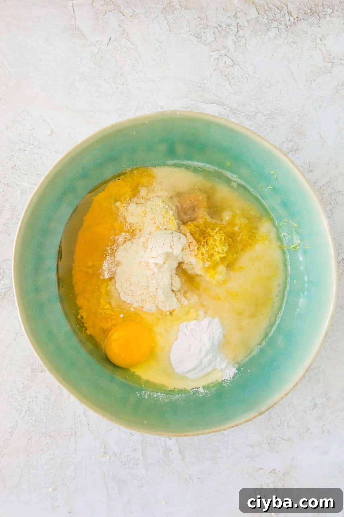 A bowl with almond flour, an egg, lemon zest, lemon juice, coconut flour and tapioca flour in it.