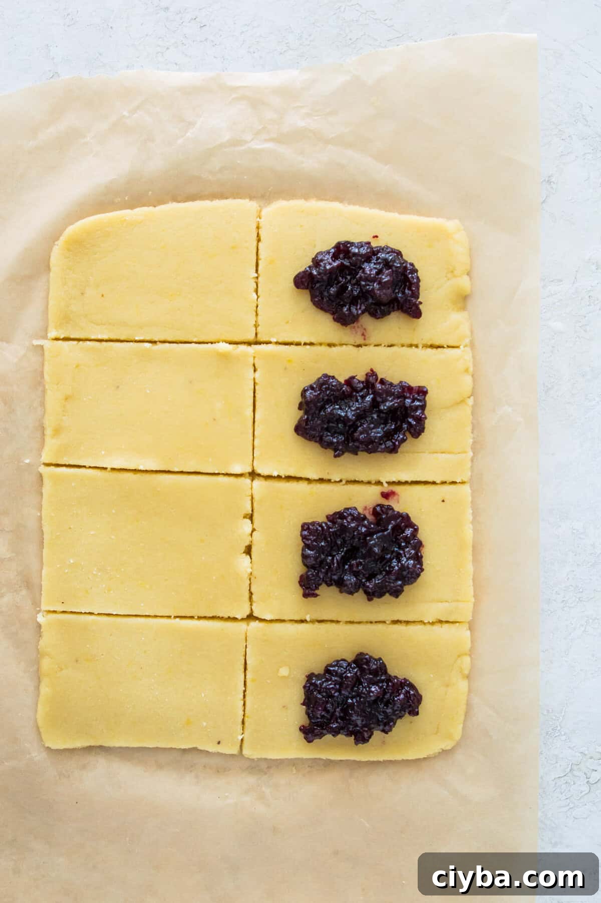 A piece of dough that has been cut into 8 evenly sized rectangles and half of them have blueberry jam on them.