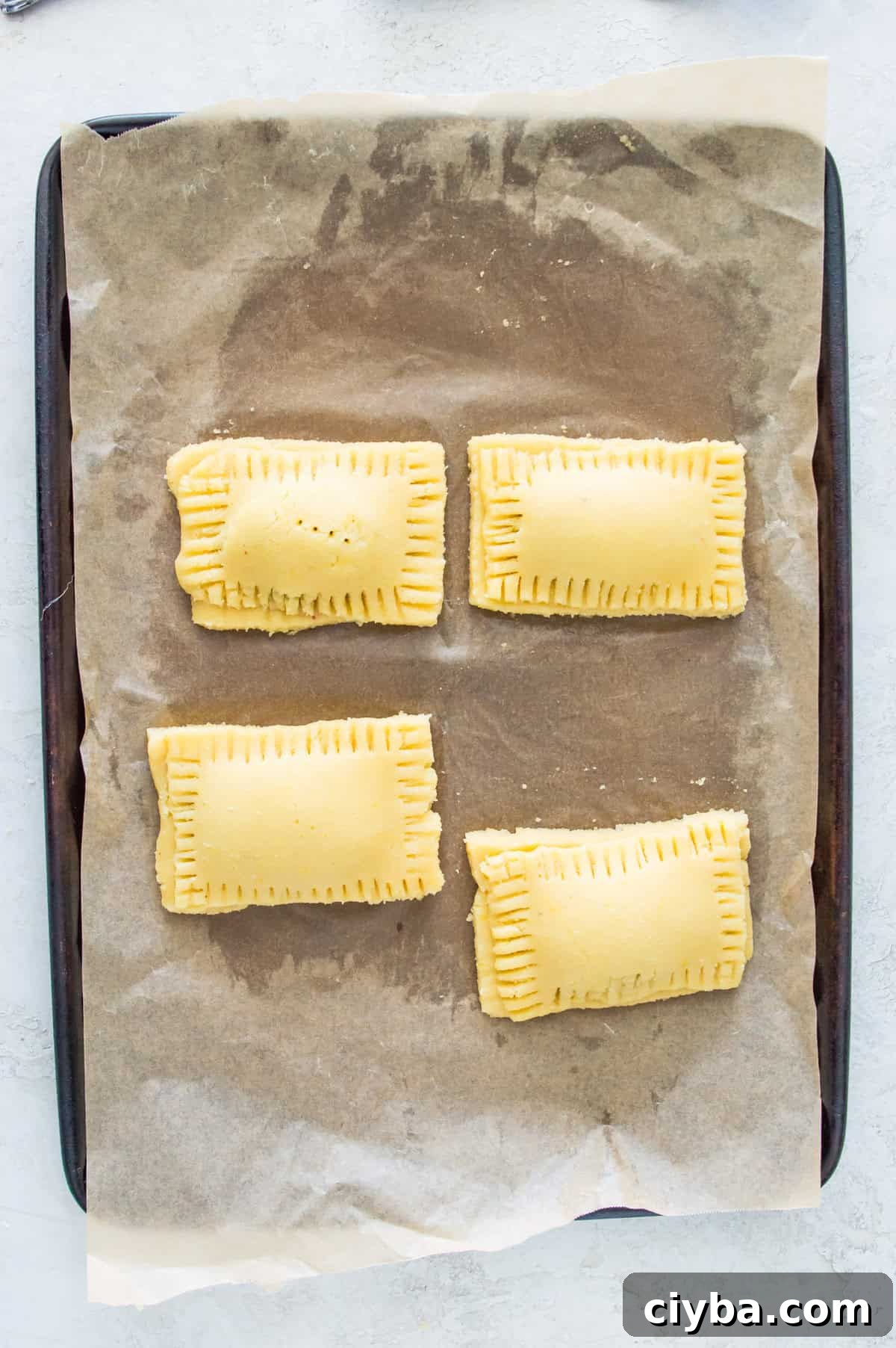 Pop tarts that have not been baked on a baking sheet lined with parchment paper.