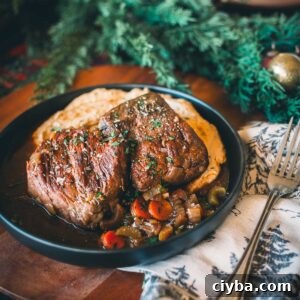 A plate with two pieces of sous vide short ribs on a bed of vegetables, garnished with herbs, next to a fork and a decorative napkin.