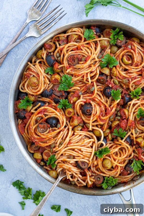 Authentic Spaghetti alla Puttanesca Recipe 3 a fork spiraling some spaghetti puttanesca in a large skillet garnished by parsley