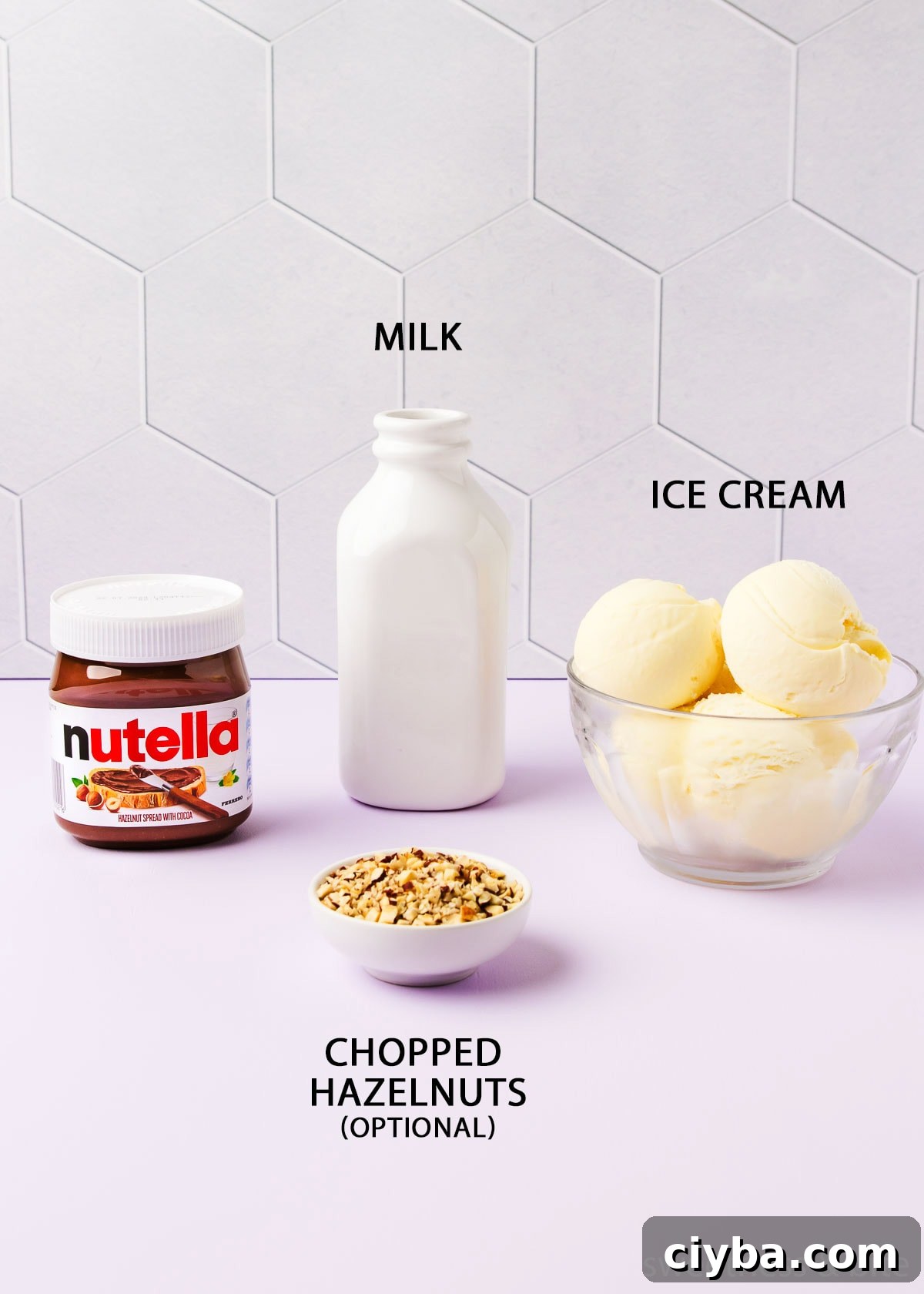 The recipe ingredients - Nutella, vanilla ice cream, milk and chopped hazelnuts, on a pale purple background.