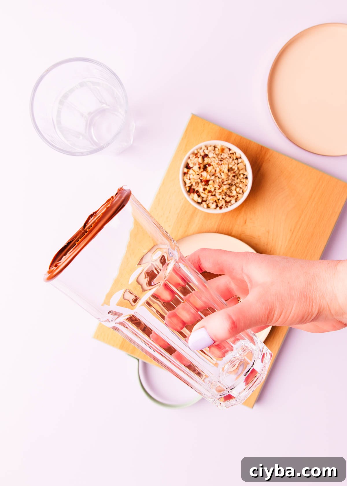 A hand holding a tall milkshake glass that has had the rim dipped in Nutella.