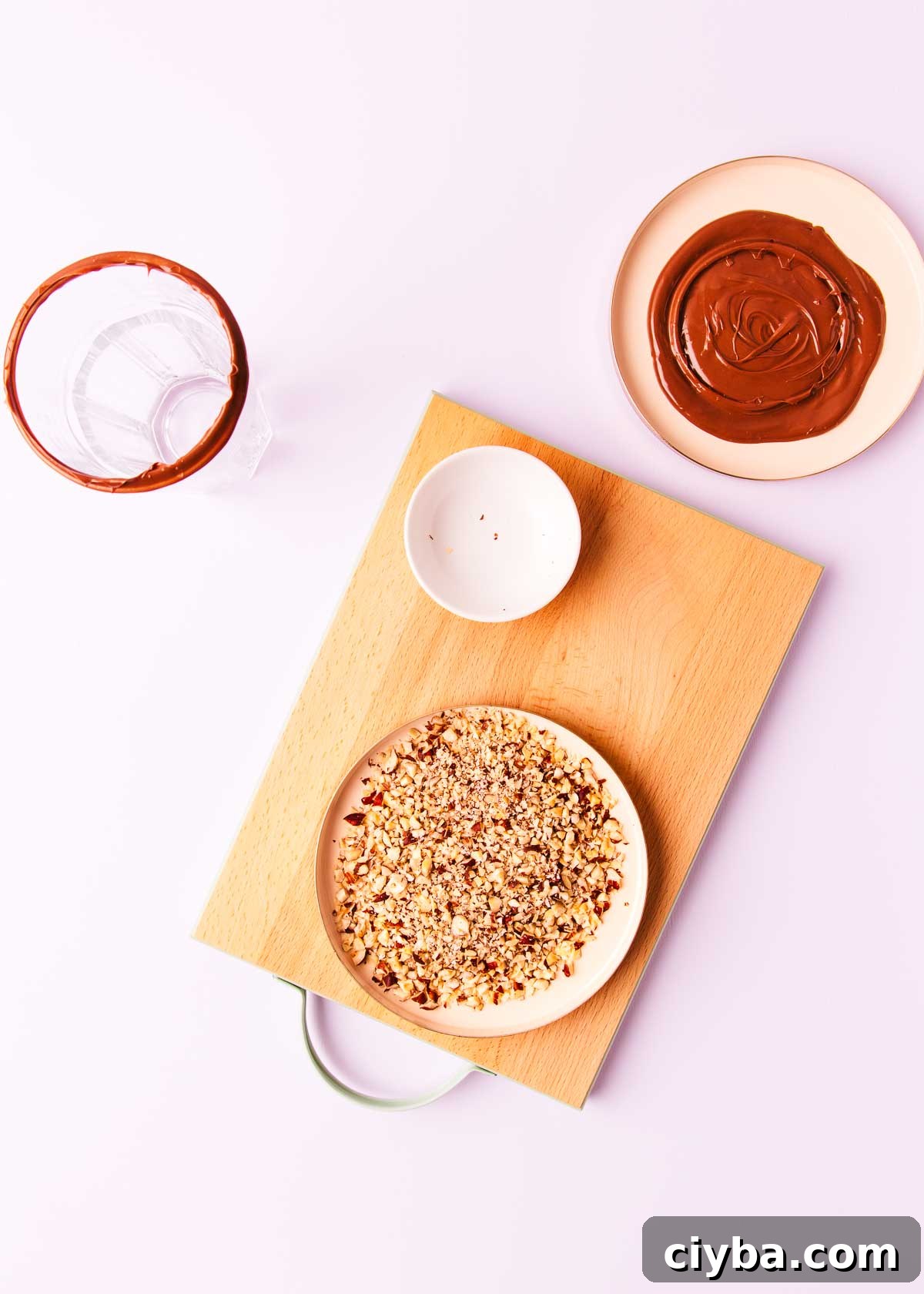 Chopped hazelnuts spread in a thin layer on a pink plate, on a pale purple background.
