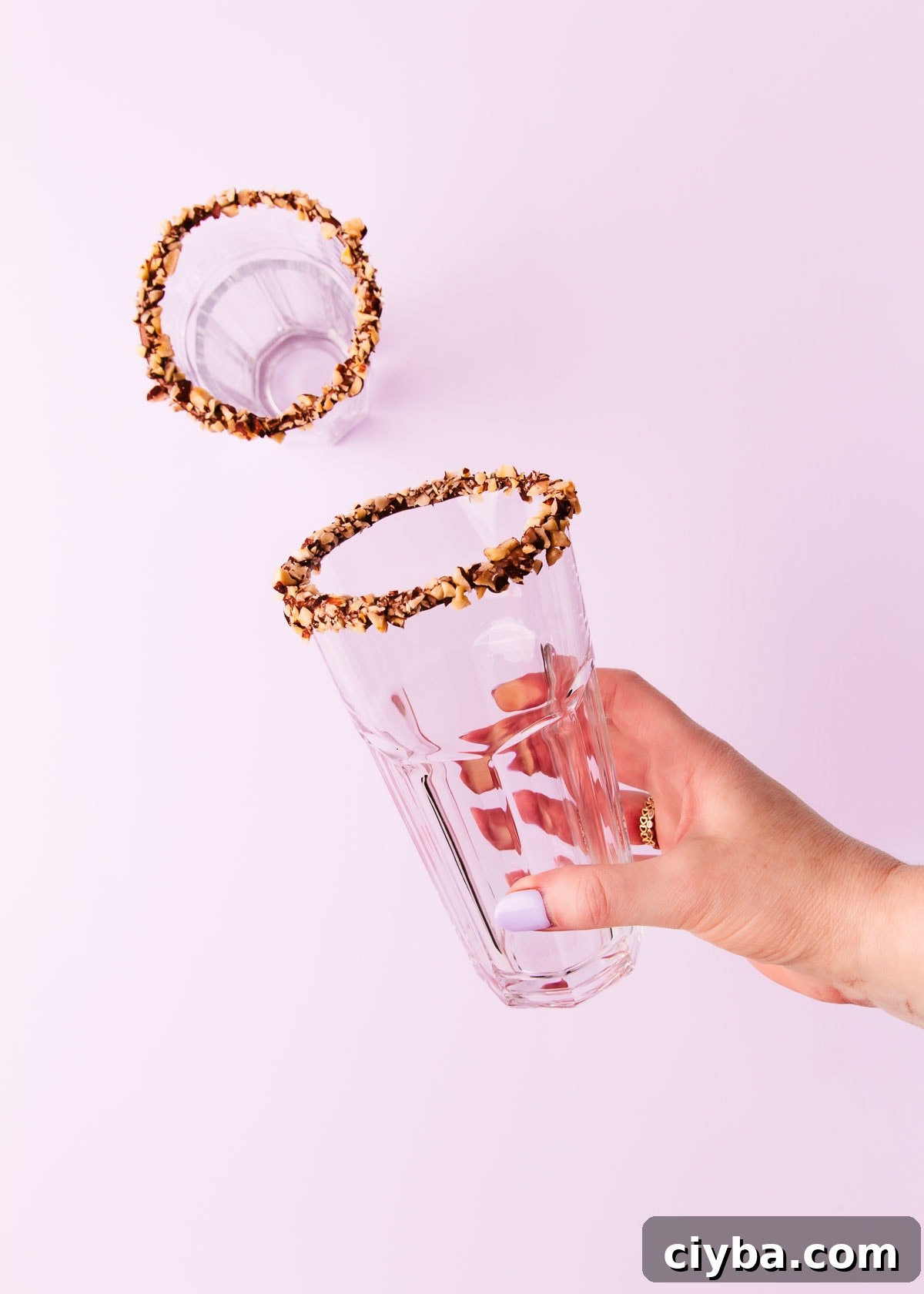 A hand holding a glass with a Nutella dipped rim covered in chopped hazelnuts.