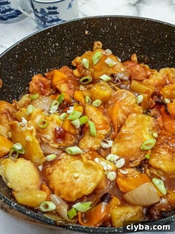 Overhead shot of a pan of sweet and sour chicken pieces garnished with spring onions.