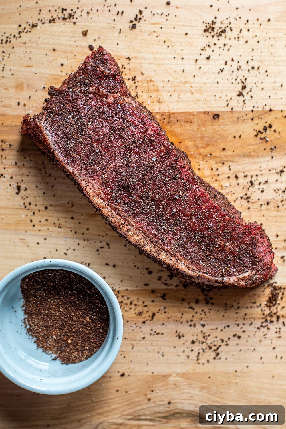 Coffee-Rubbed Steak Recipe for Tender, Flavorful Results 4 An uncooked NY strip steak seasoned with a coffee rub on a wooden cutting board.