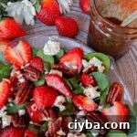 strawberry spinach salad with pecans on plate with dressing next to it