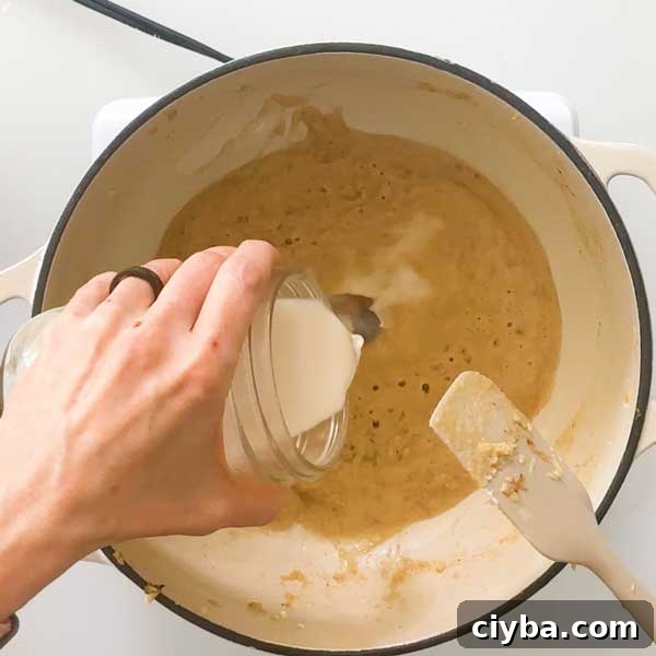 Adding almond milk to roux in pot.