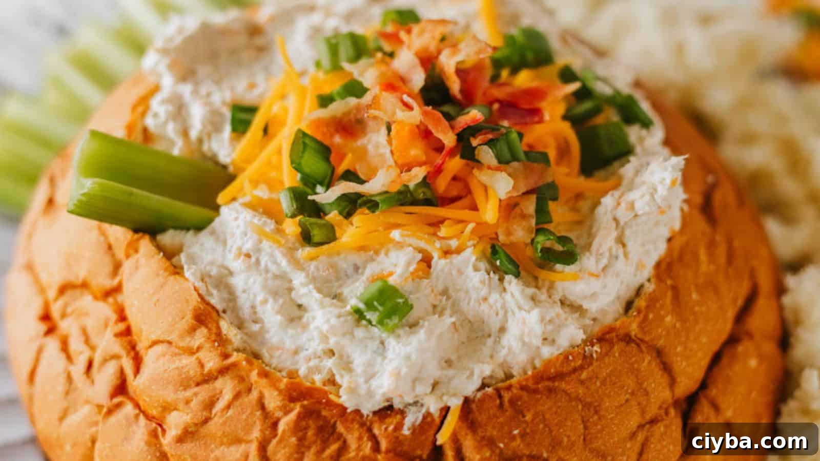 Despite a Busy Schedule, I Completed 17 Dips 18 A bread bowl filled with a creamy dip, garnished with shredded cheese, chopped green onions, and bacon bits. Celery sticks are placed on the side.