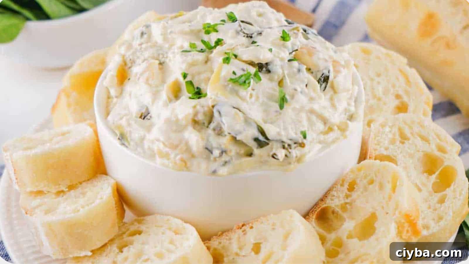 Despite a Busy Schedule, I Completed 17 Dips 4 A bowl of creamy spinach dip garnished with herbs, surrounded by slices of crusty bread on a blue patterned cloth.