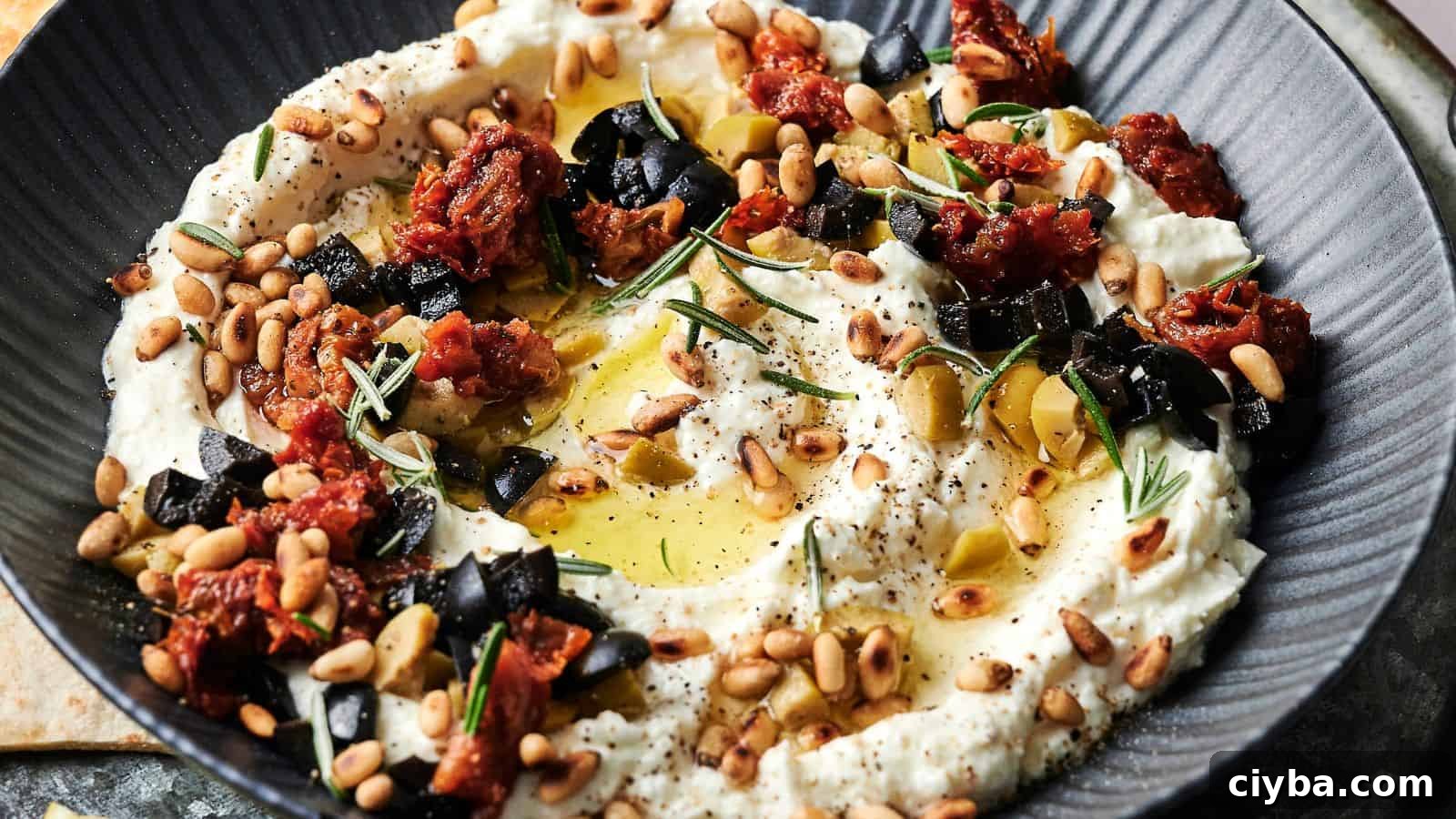 Despite a Busy Schedule, I Completed 17 Dips 10 A bowl of creamy dip garnished with chopped black olives, sun-dried tomatoes, pine nuts, rosemary, olive oil, and black pepper.