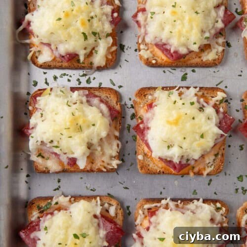 mini reuben sandwiches with a square of toasted rye bread topped with corned beef and melted swiss cheese on a sheet pan.