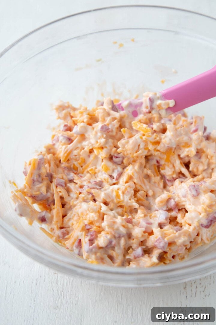 shredded cheddar and chopped pimentos in a creamy mayonnaise sauce in a mixing bowl.
