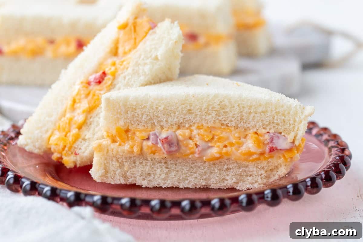pimento cheese finger sandwiches cut into triangles on a decorative plate.